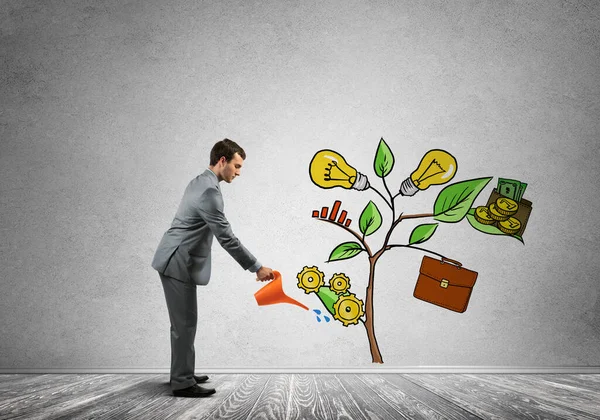 Young businessman in empty room watering drawn growth concept with can Royalty Free Stock Images