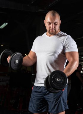 Spor salonunda dambıllarla çarpışan erkek vücut geliştirici.