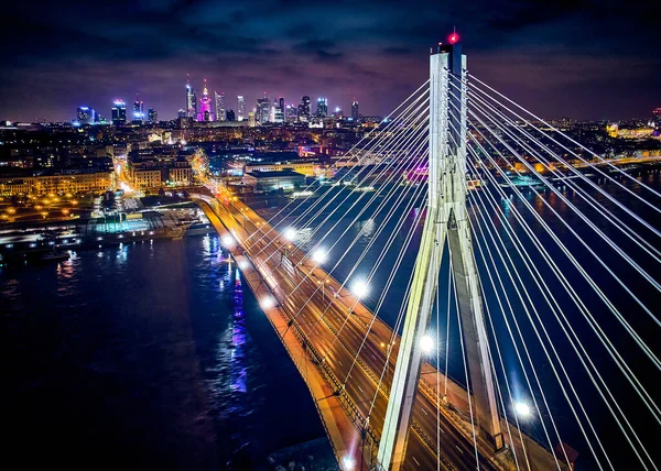 Beautiful panoramic aerial drone skyline view of the center of night Warsaw with skyscrapers in the background with the Swietokrzyski suspension bridge - the lights of the big city by night, Poland.