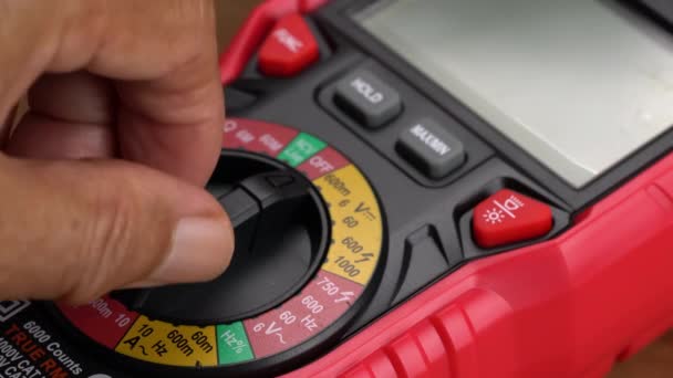 電圧を測定するための赤いマルチメータの人間の手旋削ノブのクローズアップビュー — ストック動画