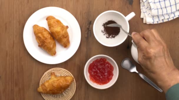 おいしい自家製クロワッサンと朝食でインスタントコーヒー粉末と白いセラミックカップにお湯を注ぐのトップビュー — ストック動画