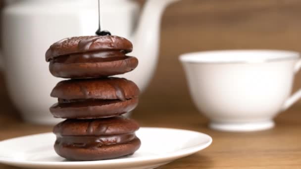 将巧克力糖浆倒入白色陶瓷盘中的巧克力派中 并在木桌上倒入一杯热茶和茶壶 — 图库视频影像