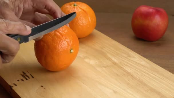 男性手を保持し 木製ボード上の2ピースにキッチンナイフで熟したオレンジを切断 — ストック動画