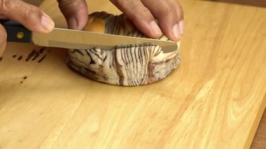 Kıdemli eller bir somun çikolatalı ekmeği ahşap kesme tahtasıyla tutuyor ve kesiyor..