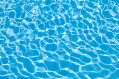 Gün ışığında yüzme havuzunda mavi berrak su dokusunun bulanık dalgalanması. Arkaplan olarak güneş ışığındaki su dalgasının görünümünü kaldır.