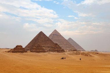 Giza Platosu 'nun manzarasında turistler ve yerli halk deve sürerken ve Büyük Piramit arka planda sisli bir günde Kahire, Mısır.