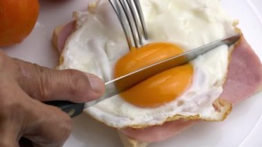 Bıçak ve çatal kullanarak jambona kızarmış tavuk yumurtası ve beyaz seramik tabakta kırmızı domatesli tost..