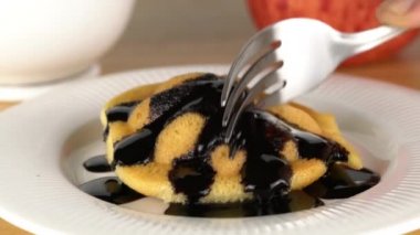 Metal çatal kullanarak beyaz seramik tabakta tatlı çikolata şurubuyla doldurulmuş ev yapımı küçük bir Castella pastası kesip....