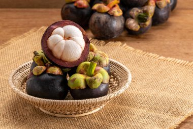 Bambu sepetindeki taze mangosteen meyveleri çuval bezinin üzerinde ve arka plandaki ahşap masanın üzerinde..