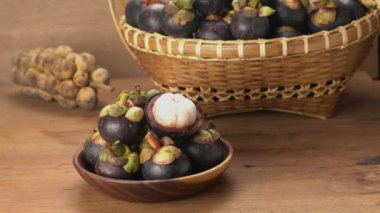 Ahşap bir tabaktaki soyulmuş mangosteen 'in yarısını alan bir adam. Arkaplanda bir sürü longkong ve bir sepet mangosteen var..