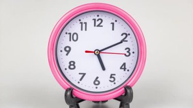 Closeup beautiful pink clock on a desk against white background, 5 o'clock, time lapse.