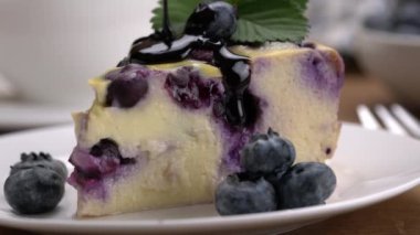 Pouring chocolate syrup onto a slice of delicious homemade blueberry yoghurt cake in white ceramic dish, closeup.