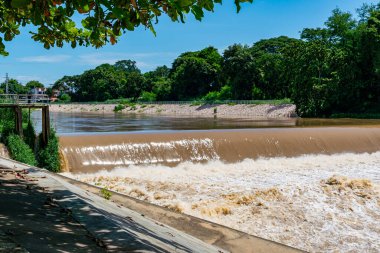 View of muddy water streams rushing rapidly on the river flowing over a weir, falling down, splashing and forming air bubbles.