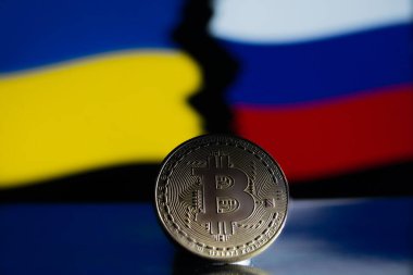Ukrayna ve Rus bayrağının arka planında metal para Bitcoin. Ekonomik yaptırımlar kavramı.