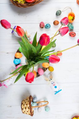 Beyaz ahşap arka planda lale ve bahar çiçekleri olan paskalya renkli yumurtalar..