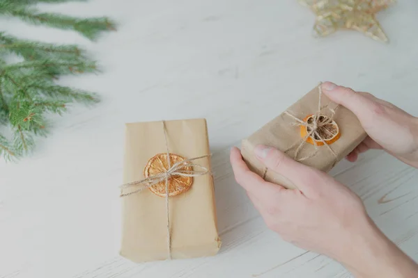 Bir adam Noel hediyesini beyaz ahşap arka planda el sanatları kağıdına sarar..