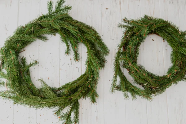 The process of creating a Christmas wreath on a white wooden background.