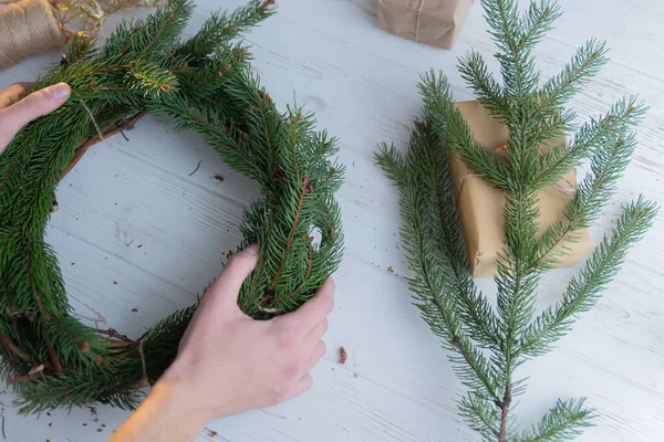 The process of creating a Christmas wreath on a white wooden background.