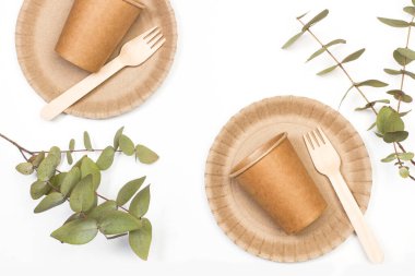 Tek kullanımlık bardaklar, tabaklar ve beyaz arka planda ahşap çatal bıçak.