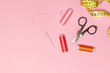 Colored thread spools and sewing accessories on a pink background in a top view
