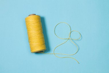 Açık mavi arkaplanda sarı iplik makarası dikiliyor