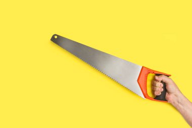 Elinde testereyle sarı bir arkaplan tutan bir adam.