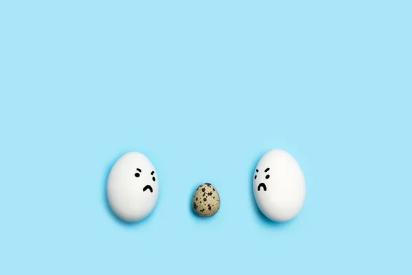 Два Яйца Сердитым Лицом Смотрящие Перепелиное Яйцо Синем Фоне — стоковое фото