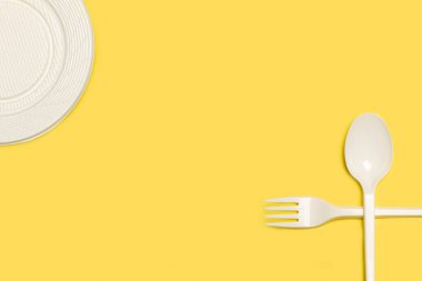 Tek kullanımlık beyaz plastikler için, sarı arka plan üzerinde kaşık ve plaka kopyalama alanı ile