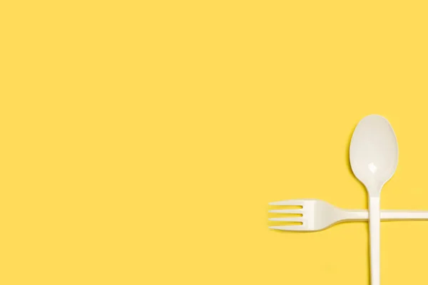 可处置的白色塑料叉子和勺子放在带有复制空间的黄色背景上 — 图库照片