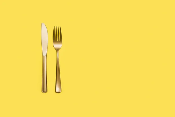 黄色背景上带有复制空间的金色塑料叉子和刀 — 图库照片