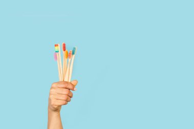 Açık mavi arkaplanda bambu diş fırçası tutan bir kadın.