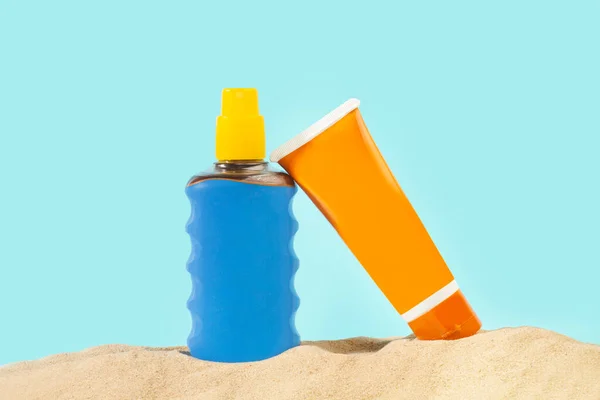 Orange and blue suntan lotion bottle on the sand and on a blue background