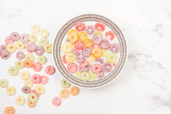 Fruit flavor colored cereals in a bowl with milk on a kitchen marble counter in a top view