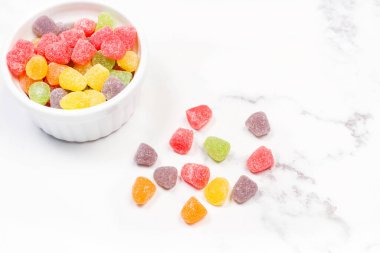 Colored gummies in a white bowl and on a marble kitchen counter