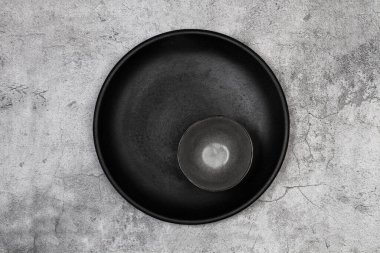 Black round dish and a dark bowl on a stone background in a top view