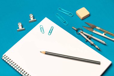 Mavi arkaplanda boş not defteri ve öğrenci gereçlerini aç