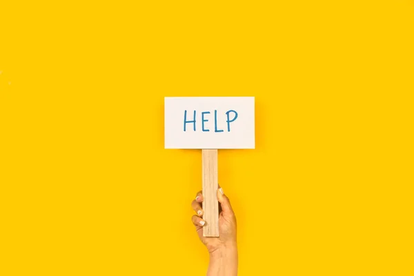 Woman hand holding a help sign on a yellow background with copy space