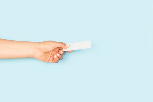 Woman hand holding a blank white personal card on a light blue backgroud with copy space