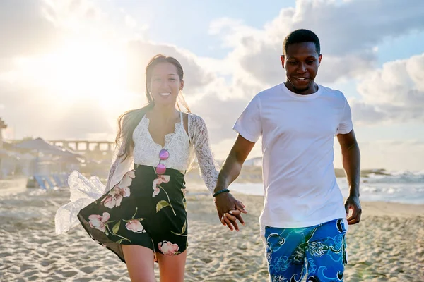 Boldog fiatal, multiracionális pár, akik együtt futnak a parton. — Stock Fotó
