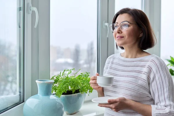 Mulher bonita de meia idade com óculos com xícara de café em casa na temporada de outono de inverno — Fotografia de Stock