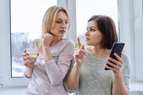 Two middle-aged women friends looking together at the smartphone screen