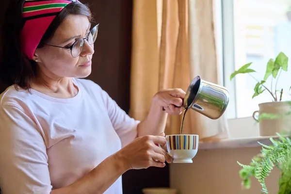 Frau mittleren Alters kocht Kaffee, gießt aus einem Cezve Türke in eine Tasse. — Stockfoto