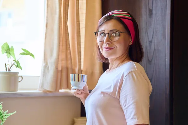 Портрет жінки середнього віку вдома на кухні з чашкою кави — стокове фото