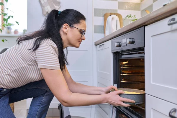 Middle aged woman cooking pie in the oven at home in the kitchen
