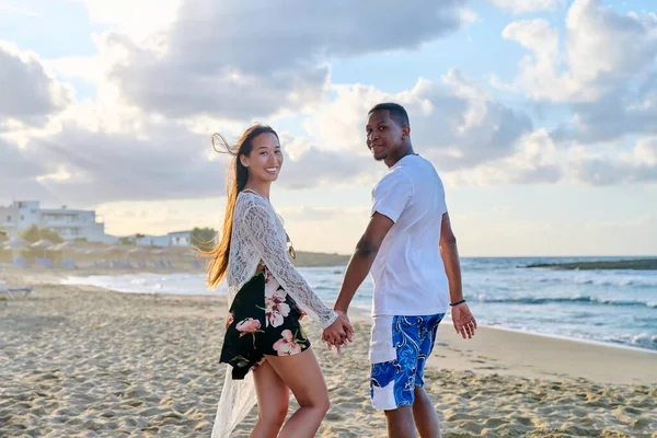 Retrato de feliz joven pareja multiétnica cogida de la mano en la orilla del mar — Foto de Stock