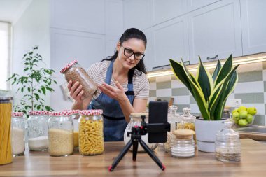 Ev hanımı evde, mutfakta akıllı telefondan video incelemesi yapıyor.