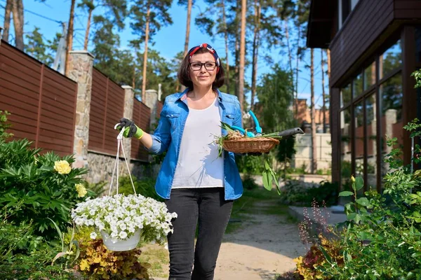 Женщина средних лет на заднем дворе с садовыми инструментами и цветущей петунией в горшочке — стоковое фото