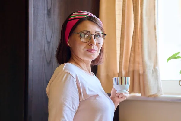 Portret van een vrouw van middelbare leeftijd thuis in de keuken met een kopje koffie — Stockfoto