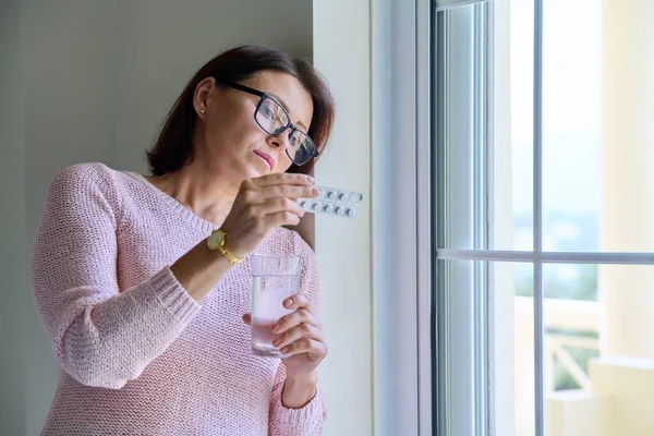 Mujer de mediana edad con pastillas y vaso de agua en las manos, en casa — Foto de Stock
