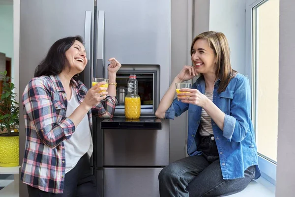 Дві жінки середнього віку друзі п'ють апельсиновий сік на кухні — стокове фото